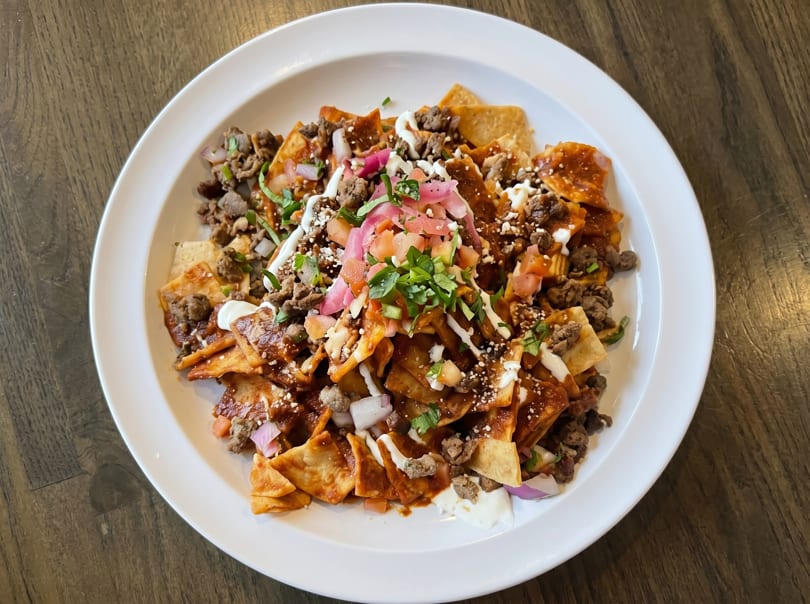 A plate of chilaquiles with red sauce, ground beef, sour cream, pickled onions, and cilantro.