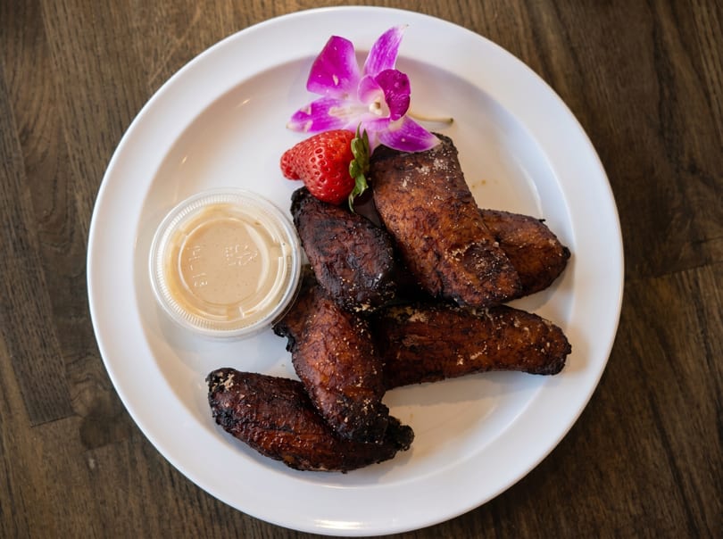 Crispy fried chicken wings with dipping sauce, a strawberry, and an orchid on a white plate.