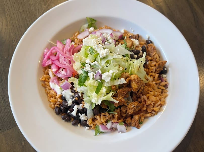 A colorful rice bowl with chicken, black beans, lettuce, pickled onions, and feta cheese.